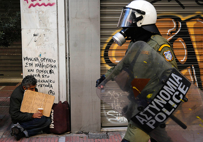 20 Photos: a riot policeman walks by a homeless beggar in Athens