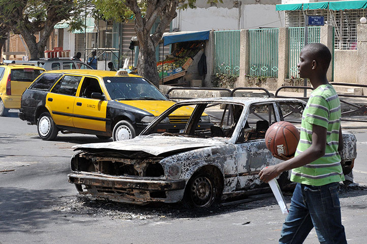 Protest in Senegal: A young Senegalese walks past a car which was burnt after clashes 