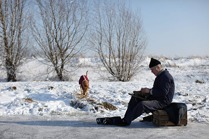 UK weather: A man puts on his ice-skates as he prepares to skate on a frozen fen 