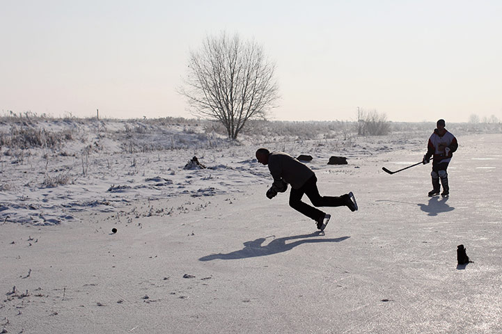 UK weather: A man falls over whilst playing a game of ice hockey on a frozen fen