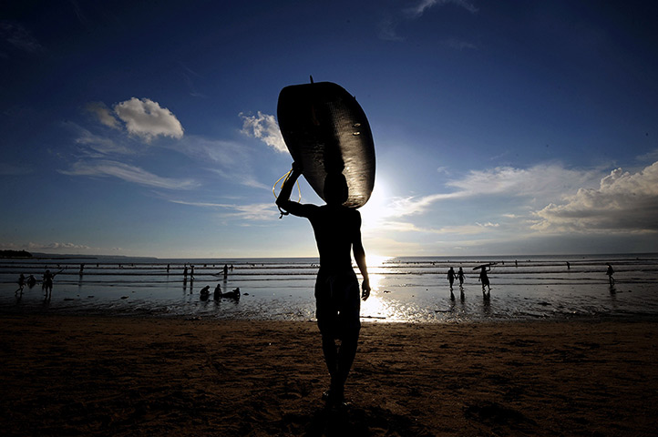 24 hours in pictures: A surfer carries a surf board at Kuta beach in Bali 