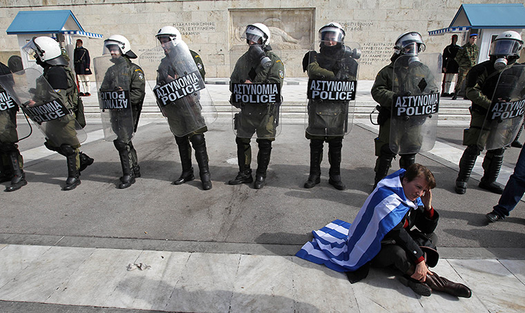 24 hours in pictures: A protester wearing a Greek flag sits in front of riot police