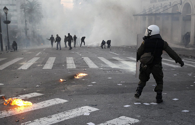 Athens demo: A riot police officer runs past demonstrators