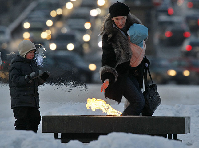 Europe weather: A woman and children warm their hands at Liberty Monument, Russia