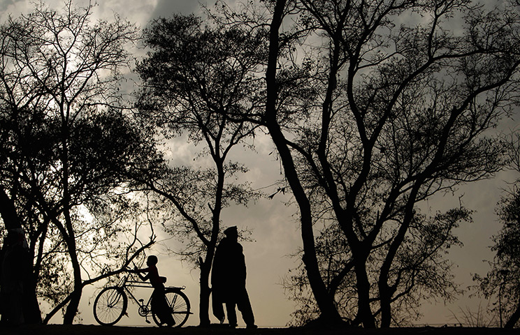 24 hours in pictures: A Pakistani boy pushes his bicycle past a man standing on a roadside