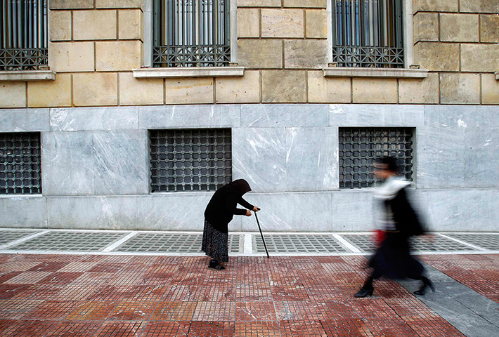24 hours in pictures: A woman beggar walks by the Bank of Greece