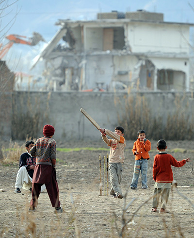 bin laden compound: Local boys play cricket as the demolition work continues in the background