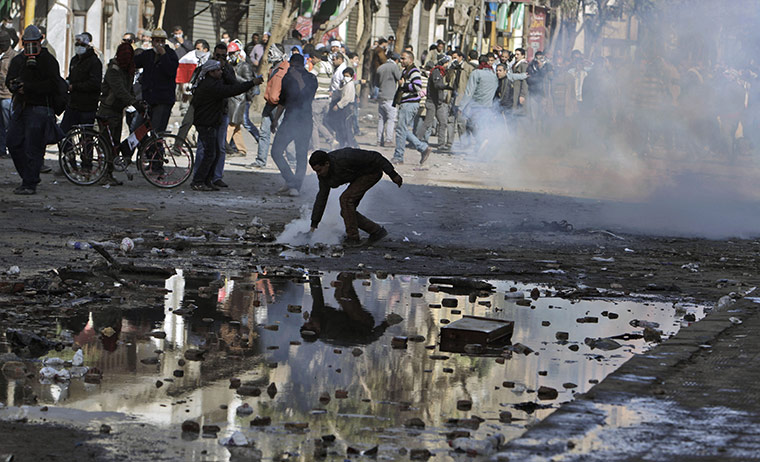 Egypt clashes: A protestor reaches for a tear gas canister fired by security forces