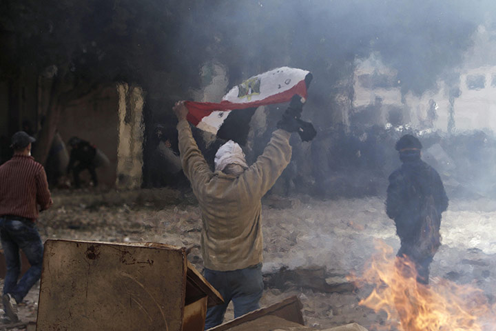 Egypt clashes: A protestor is seen through heat waves from a fire as he raises the flag