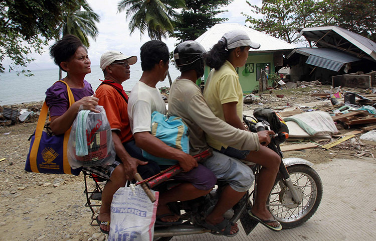 Philippines earthquake: Residents ride a motorcyle past a house destroyed by an earthquake