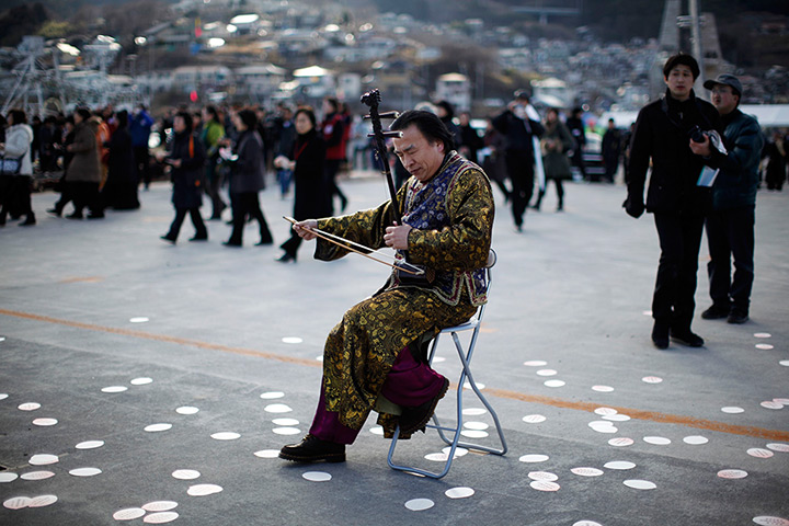 Japan anniversary: A musician performs as local residents prepare to observe moment's silence