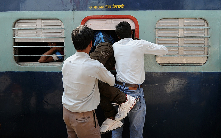 24 hours in pictures: Indian men help a commuter get inside a train at New Delhi Railway Station