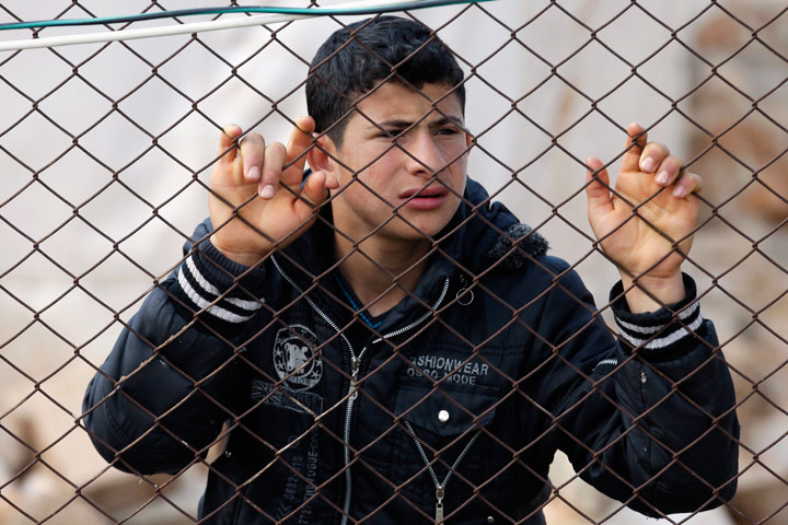 Syrian Refugees: A Syrian refugee boy stands behind a fence 