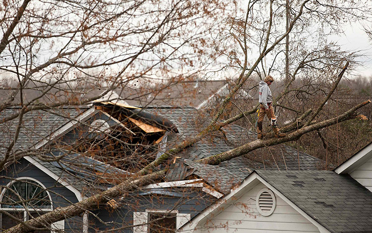 Midwest tornado: A worker stands on a downed tree that rests on a home in Charlotte