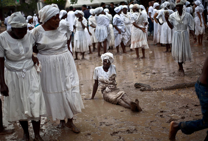 Haiti - A longer view: A Voodoo believer sits on the mud during the ceremony in Souvenance, Haiti