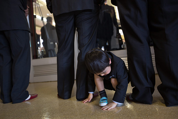 Kawauchi, Japan: A young boy plays in amongst the legs of elder men