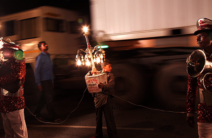 24 hours: Bijnor, India: A young Indian boy holds a light at a wedding procession
