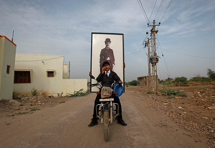 From the Agencies: A man drives a motorbike with a passenger holding a portrait of Chaplin
