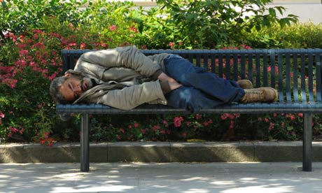 A vagrant sleeping on a public bench in the summer