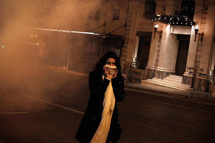 Greece unrest: A woman covers her face after inhaling tear gas