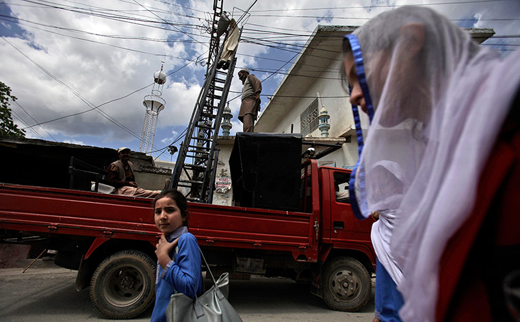 Abbottabad one year on: Schoolgirls walk by municipality workers fixing electrical wires