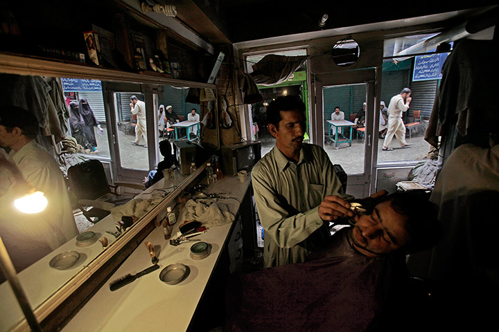 Abbottabad one year on: Barber lights his shop with a lamp in a power cut, while shaving a customer