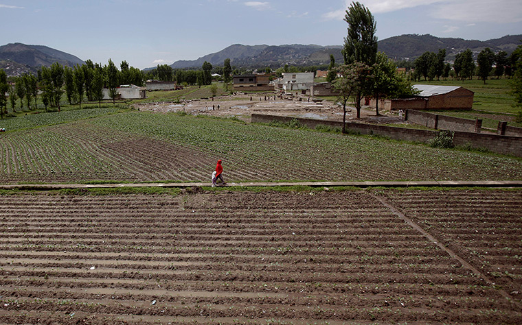 Abbottabad one year on: A woman and a girl walk through a field next to the demolished house 