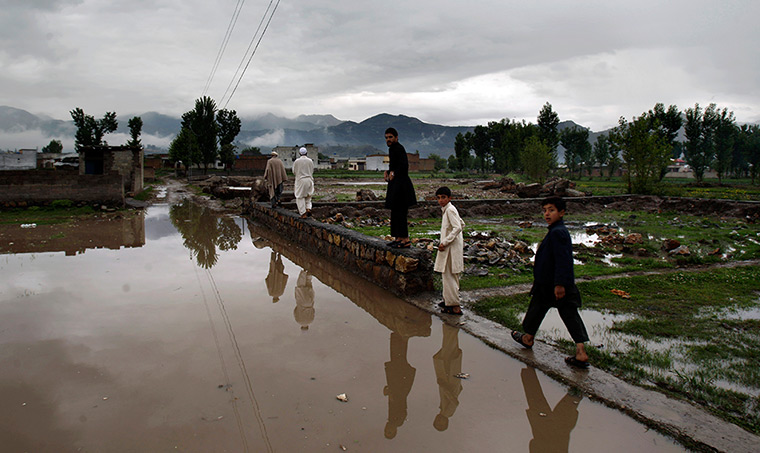 Abbottabad one year on: Men walk on the edge of the flooded road toward the demolished compound