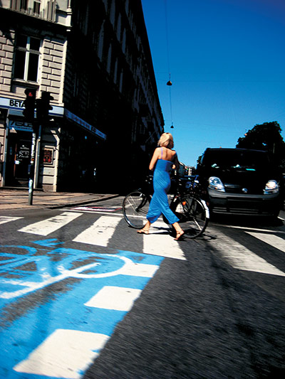 Big Picture, bikes: Big picture: Woman walking a bike across a blue crossing also wearing blue