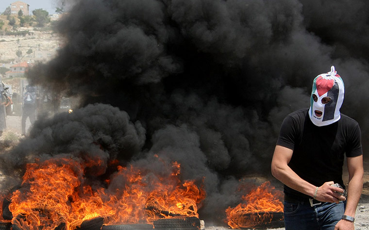 Picture desk live: A masked Palestinian protester stands near burning tyres 