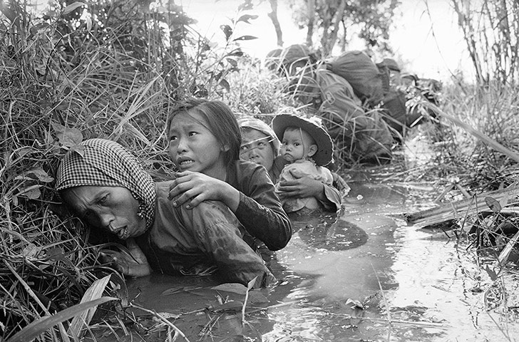 Horst Faas gallery: Women and children crouch in a muddy canal