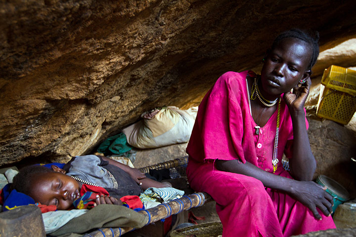 Nuba Mountains Conflict: A mother rests with her child in a cave outside of Tess