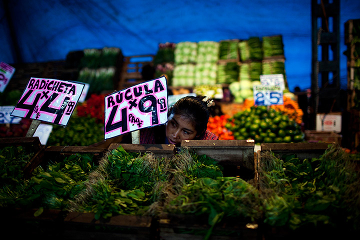 24 hours in pictures: A vegetable vendor peeks out from a sign promoting arugula at a market