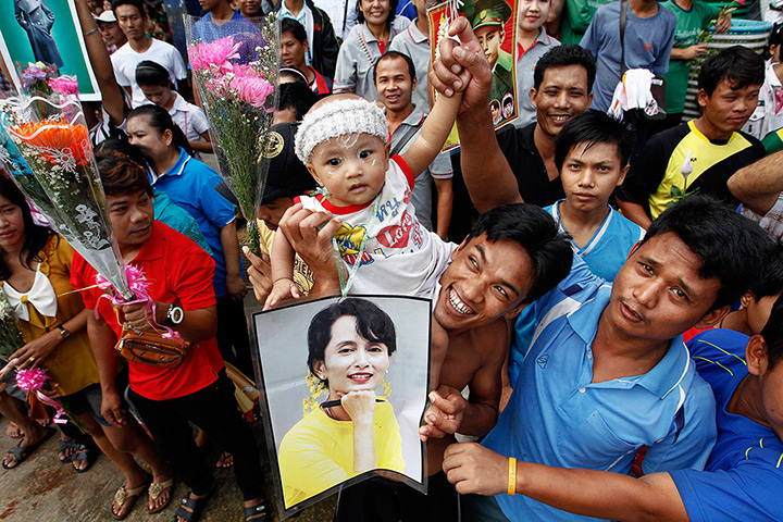 Suu Kyi visits Thailand: Migrant workers from Burma hold up pictures and flowers in Samut Sakhon 