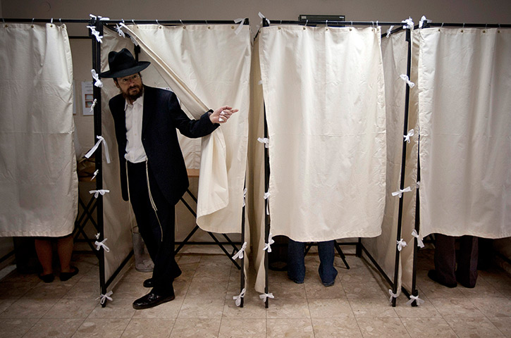 24 hours in pictures: An Ultra Orthodox Jewish man opens a curtain of a voting booth, Tel Aviv