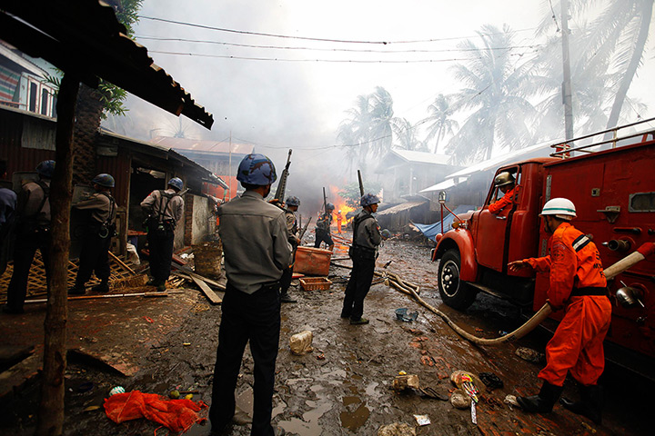 Myanmar violence: Policemen stand guard as firemen work to extinguish fire during fighting