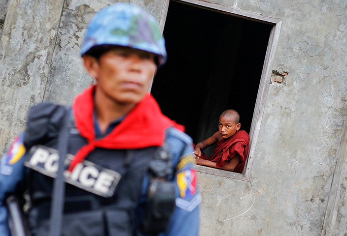 Burma violence: A Buddhist monk looks from the window behind a policeman in Sittwe