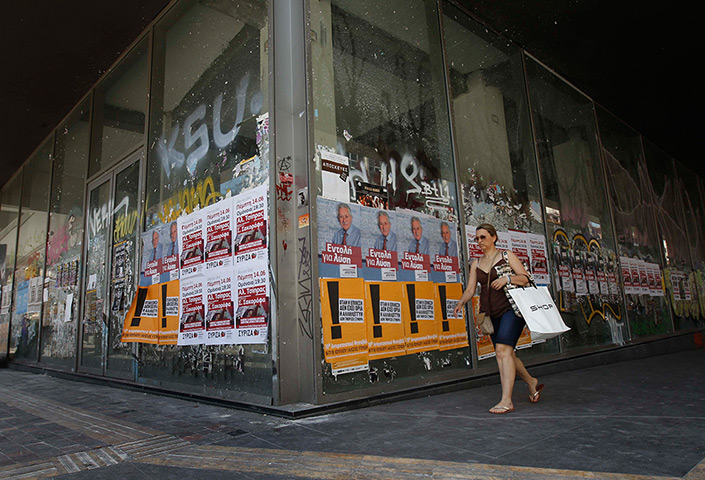 Greece: 13-14 June: A woman walks past a closed shop plastered with election campaign posters