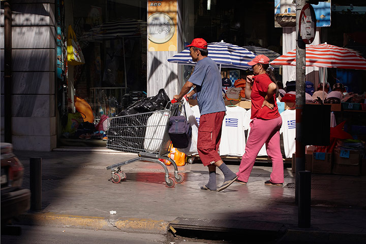 Andy Hall Athens: A couple walk across town with their possessions in a shopping trolley