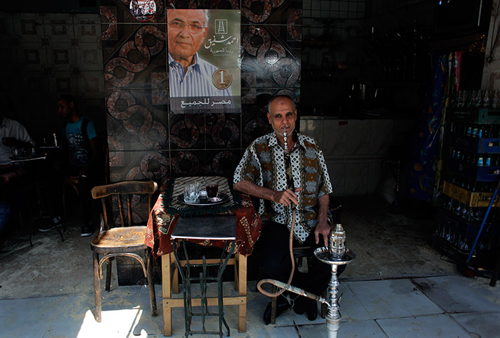 Egypt elections day 2: An Egyptian man smokes a water pipe under a poster of Ahmed Shafiq 