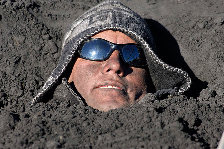 24 hours in pictures: A local resident buries himself into an ash deposit during a protest