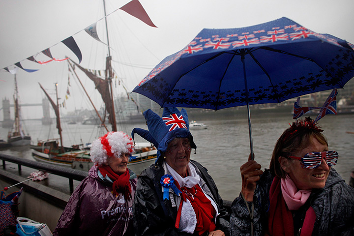 Jubilee pageant: People wait beneath an umbrella in the rain near Tower Bridge