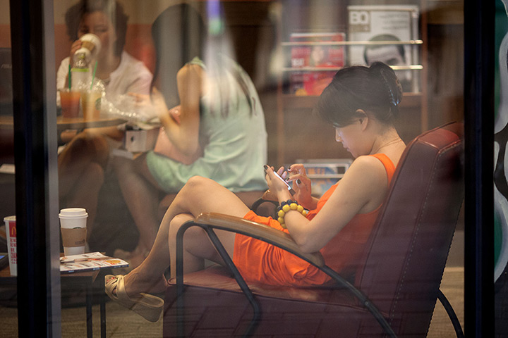 Week in Business: A woman looks at a smartphone as she sits in a cafe in Beijing