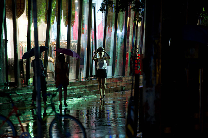 24 hours: Beijing, China: A woman covers her head as she walks during heavy rainfall 