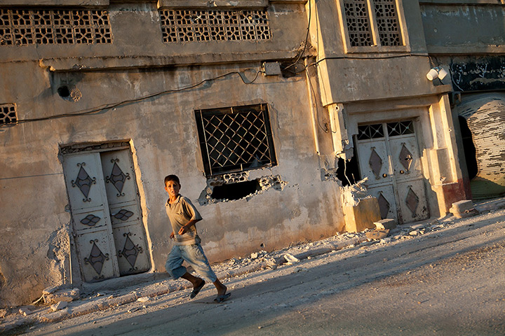 Tremseh, Syria: A boy runs past damaged houses