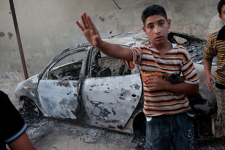 Tremseh, Syria: A youth gestures in front of a burnt car