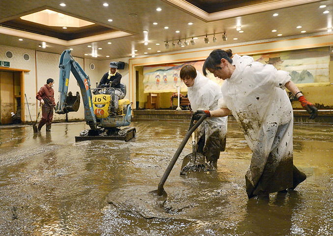 Floods in Japan: Workers shovel muddy water out of a banquet room of a hotel in Aso