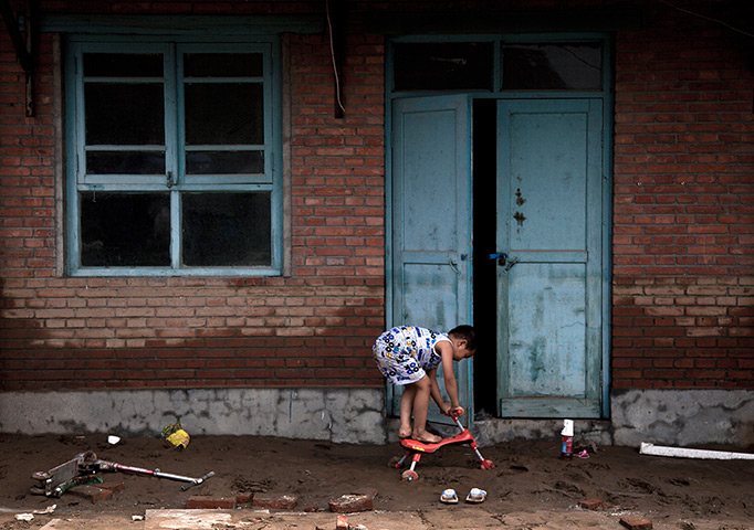 24 hours in pictures: A child plays on the mud outside his flood hit house at a village, China