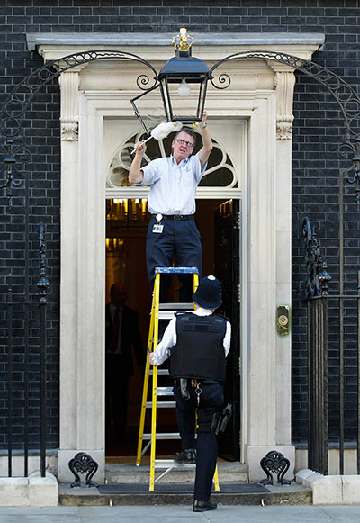 Queen and PMs: A policeman holds the ladder for a cleaner