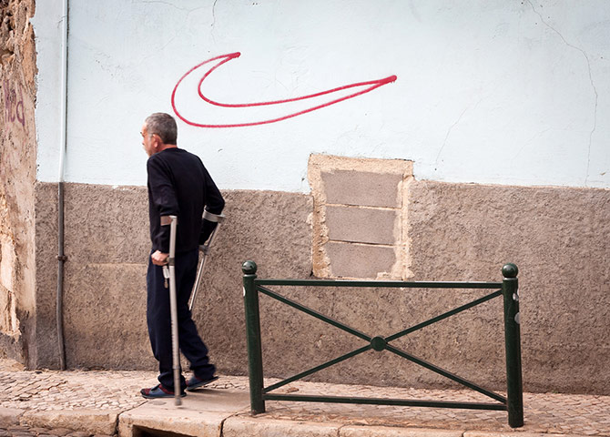 Your Pictures: Run: A man in crutches nest to a graffitied Nike tick sign